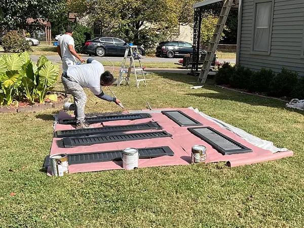 man painting window shutters outside of home on lawn