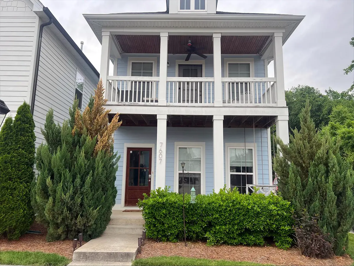 a light blue and white house with a porch and a brown door
