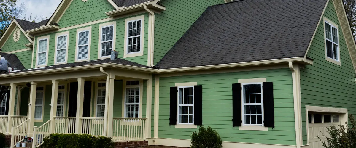 Freshly painted green house exterior with cream trim and black shutters after professional residential house painting service