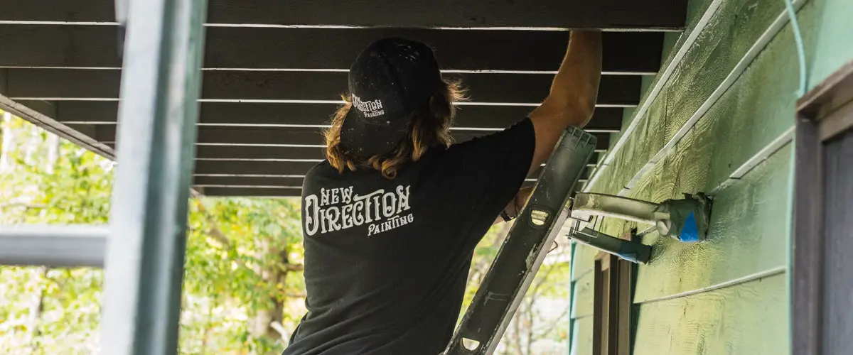 Painter from New Direction Painting working on a black ceiling under outdoor deck during home exterior repaint